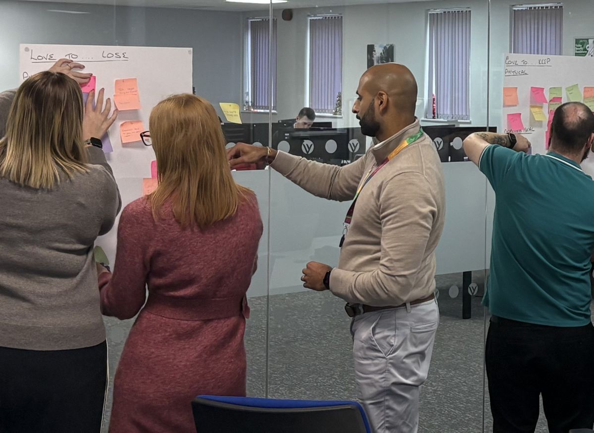 A team placing sticky notes on a glass wall under Love to lose and Love to keep headings